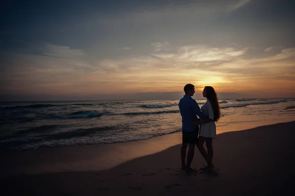 Two young lovers standing on a beach and looking to each other on sunset background.sillhouette couple love — Stock Photo, Image