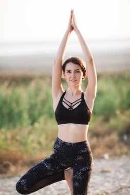 Genç bir kadın tarafından Sunset.Vrikshasana plajda Yoga uygulamak. Ağaç poz