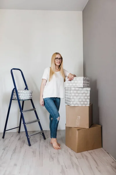 Young woman moving in her new house and doing a home makeover, she is standing near many cardboard boxes around