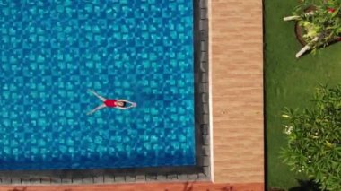 Kırmızı bikinili ince genç kadının üstte, kristal berraklığında suda yüzen arkada yüzen ve yüzme havuzunda dinlenen. Güneşin tadını çıkarıyorum. Tatil konsepti. Hava veiw. Drone