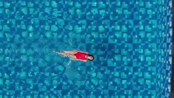 Top view of slim woman in red bikini swimming on back and relaxing in blue swimming pool. Vacation concept. Aerial veiw. Drone — Stock Video