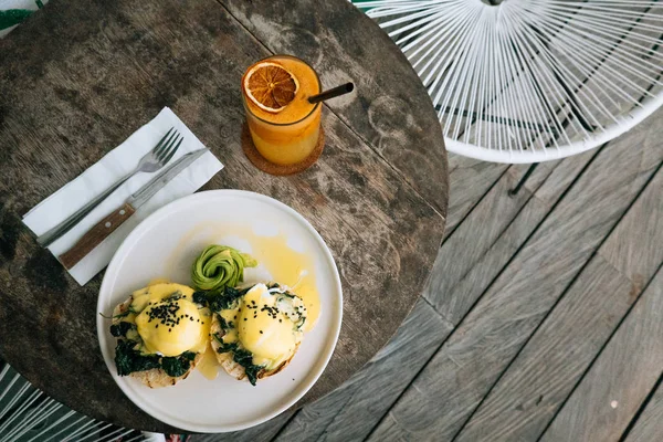 Top utsikt över hälsosam frukost med bröd toast och pocherat ägg med spenat, avokado på träbord. Apelsin smoothie på bakgrunden. — Stockfoto