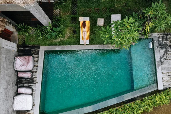 Vista superior de la joven delgada irreconocible en bikini beige relajante y tomar el sol cerca de la piscina de lujo en el trópico verde en Ubud.Concepto de vacaciones. Drone foto —  Fotos de Stock