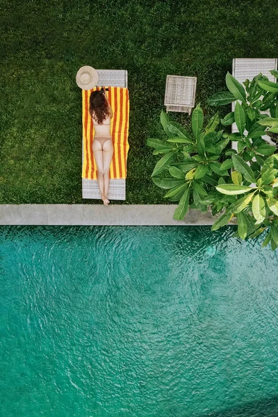 Draufsicht auf eine unkenntlich schlanke junge Frau im beigen Bikini, die sich in der Nähe des Luxus-Swimmingpools im grünen Tropenwald in Ubud entspannt und sonnt. Drohnenfoto — Stockfoto