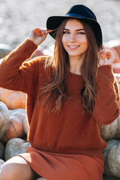 Porträtt av lycklig kvinna som sitter på marknaden med orange pumpa i brun tröja och hatt. Mysiga höstvibbar Halloween, Thanksgiving dag. — Stockfoto