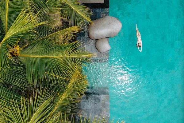 Vue aérienne de la jeune femme mince en bikini nageant dans la piscine de luxe et les palmiers. Photo de drone — Photo