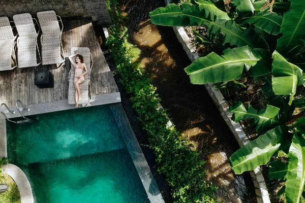 Luftaufnahme von schlanken jungen Frau im beigen Bikini entspannen und sonnen sich in der Nähe von Luxus-Pool in grünen Tropen in ubud.holiday Konzept. Drohnenfoto — Stockfoto