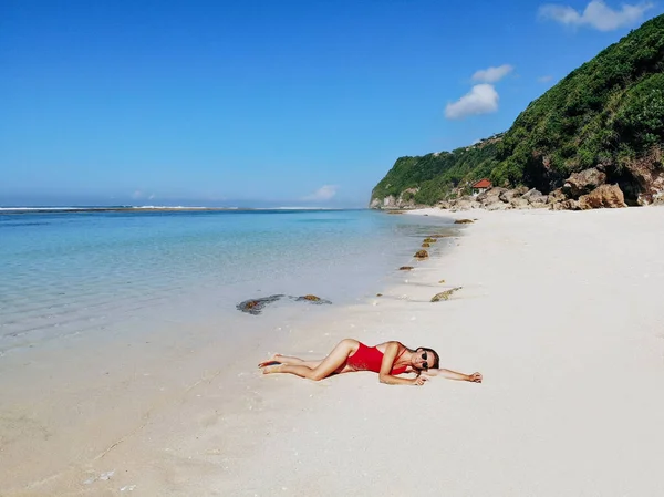 Sexy vrouw in rode bikini ontspannen op wit zand tropisch strand met blauw helder water en jungle. Bali Indonesia. Tropische achtergrond en reis concept — Stockfoto