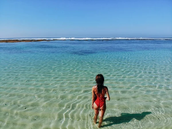 Visão traseira da mulher sexy com bunda em biquíni vermelho de pé em água clara azul na praia de areia branca. Bali Indonesia. Fundo tropical e conceito de viagem — Fotografia de Stock