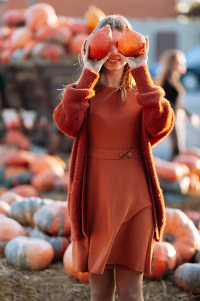 Ritratto di donna felice con zucche arancioni mature in mano chiudere gli occhi vicino al carro con zucca arancione sul mercato contadino in maglione marrone, vestito. Accoglienti vibrazioni autunnali Halloween, giorno del Ringraziamento — Foto Stock