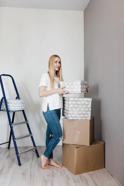 Young woman moving in her new house and doing a home makeover, she is standing near many cardboard boxes around