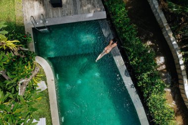 Bali 'de sonsuz havuzda dinlenen bej bikinili tanınmayan bir kadın palmiye ağaçlarının güzel manzarasına hayran. Lüks tatil. Bali adasında dinlenen bir kız. Uzayı kopyala Tatil kavramı