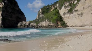 Deniz taşları ve turkuaz okyanusla okyanusa doğru yürüyen güzel bir kadın, mavi gökyüzü. Atuh Sahili, Nusa Penida Adası, Bali, Endonezya. Tropik arka plan ve seyahat kavramı. 