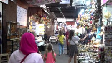 Fas, Marakeş - Ekim 2019: Medine 'de yerel pazar satıcıları ve turistlerin yürüdüğü sokak. Geleneksel hediyelik eşya ve gümüş fener dekoru seçen bir kadın.