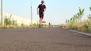 Kaykay parkında kaykayla gezen bir adamın yüz görüntüsü. Şapkadaki yaz tatili hipster 'ı kaykaya binerken bacaklarının tam uzunluğundan 4K' ya kadar.