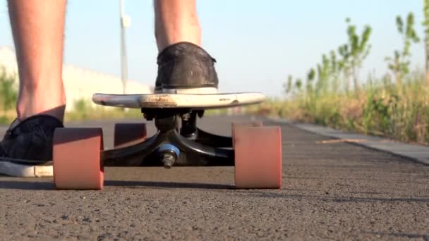 Låg vinkel, Närbild ben börjar rida skateboard på asfalterad väg vid solnedgången. Manliga ben skridskor hans longboard i solnedgången Sommar fritid koncept. Aktiv utomhussport. — Stockvideo