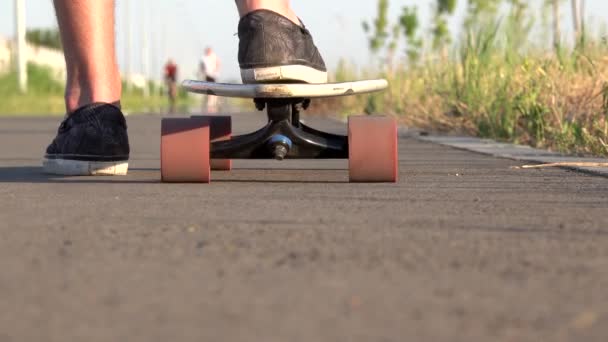 Patinadores piernas masculinas moviéndose hacia adelante longboard de cerca en ángulo bajo montar en monopatín en carretera de asfalto al atardecer. Concepto de ocio de verano. Deporte activo al aire libre . — Vídeos de Stock