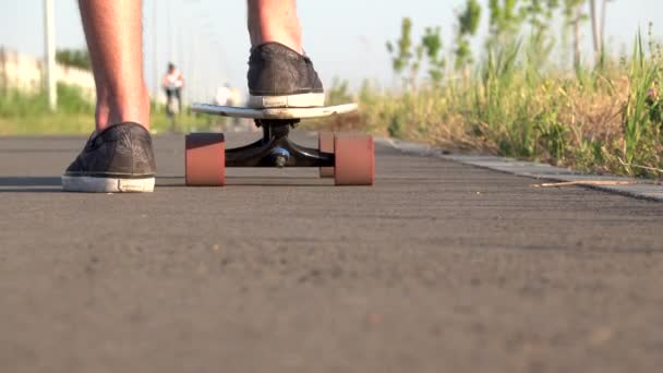 Låg vinkel, Närbild ben ridning på skateboard i rörelse av asfalt vid solnedgången. Manliga ben skridskor sin longboard på vägen i solnedgången Sommar fritid koncept. Aktiv utomhussport. — Stockvideo