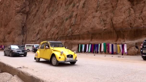 Morocco, Todra - October 2019: Vintage yellow car is driving on mountain road in a dry hot desert on a sunny day. Against the background of red cliffs. — Stock Video