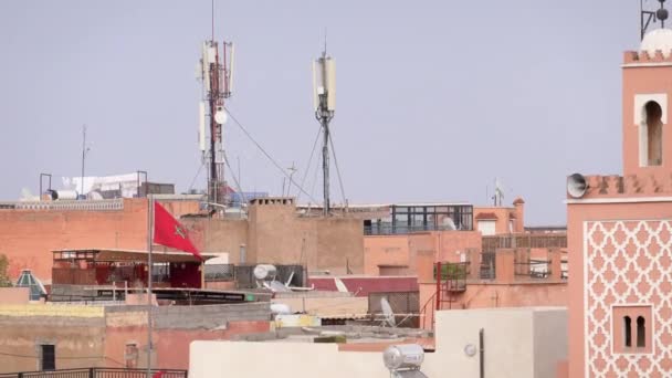 Marokko, Marrakesch - Oktober 2019: Die marokkanische Nationalflagge weht über traditionellen arabischen Gebäuden im Freien, das Symbol des Landes über der Skyline der Stadt bei sonnigem Wetter — Stockvideo