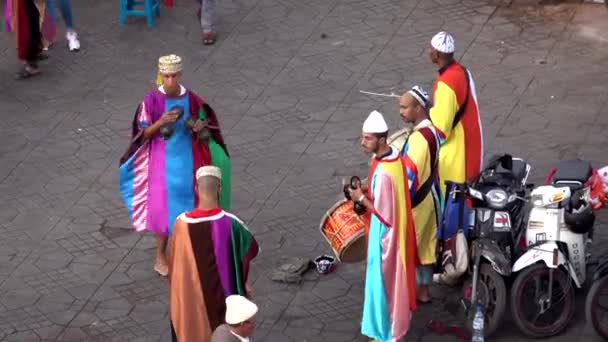 Marrocos, Marraquexe - outubro 2019: artistas de rua berbere árabes locais em roupas multicoloridas brilhantes tocando bateria e dançando fora no mercado de rua Praça Jemaa el-Fna — Vídeo de Stock
