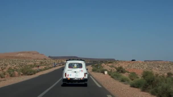 Marrocos - Outubro 2019: Tiro aéreo de carro retro dirigindo ao longo da estrada da estrada do deserto entre a natureza selvagem atmosférica perto de colinas rochosas e céu azul — Vídeo de Stock