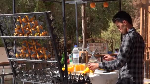 Μαρόκο, Todra - Οκτώβριος 2019: Μαροκινός τύπος συμπιέζει χυμό πορτοκαλιού με το χέρι αποχυμωτή, κάνοντας ένα πλήρες ποτήρι φρέσκο χυμό πορτοκαλιού σε ένα μαροκινό δρόμο stall — Αρχείο Βίντεο