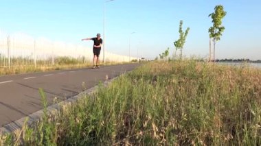 Adamın boş düz yolda oturup güneş gözlüklerine dokunuşunu görmek. Yaz tatili hippileri gün batımında şehir dışında kaykay sürerler.