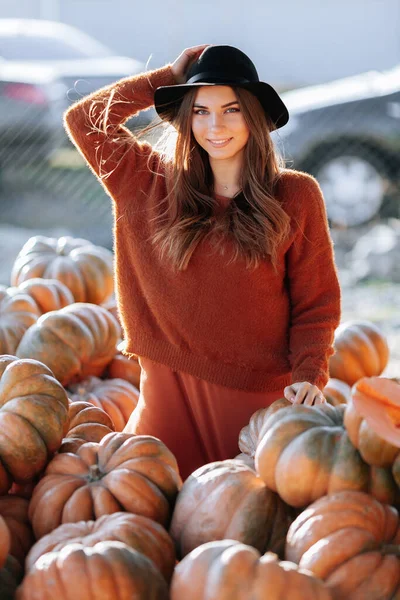 Porträtt av lycklig kvinna med mogen orange pumpa i händerna på bakgrund av jordbrukare marknaden i brun tröja och hatt. Mysiga höstvibbar Halloween, Thanksgiving dag. — Stockfoto