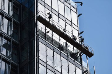 İnşaat işçileri bir gökdelen cam cephe üzerinde askıya alınmış bir platformda