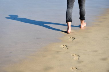 Yalınayak yapım ayak kuma bir kumsalda yürüyen adam