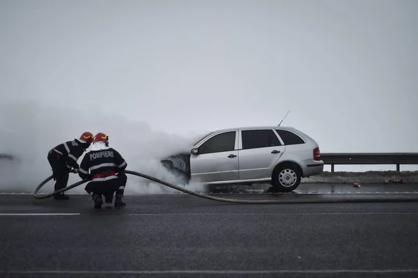 Bombeiros extinguem um carro em chamas em uma estrada — Fotografia de Stock