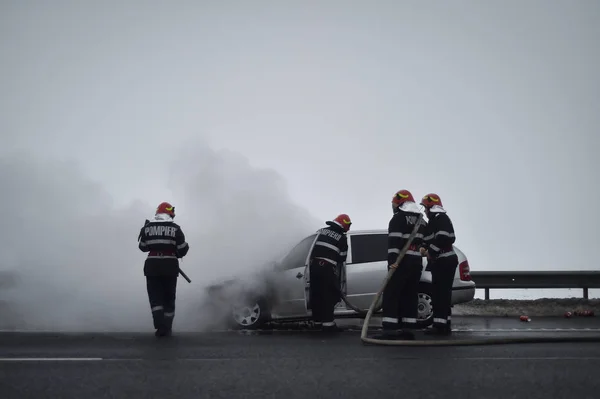 Bombeiros extinguem um carro em chamas em uma estrada — Fotografia de Stock