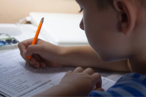 Home education. Home work after school. Boy  with pen writing english test by hand on traditional white notepad paper. — Stock Photo, Image