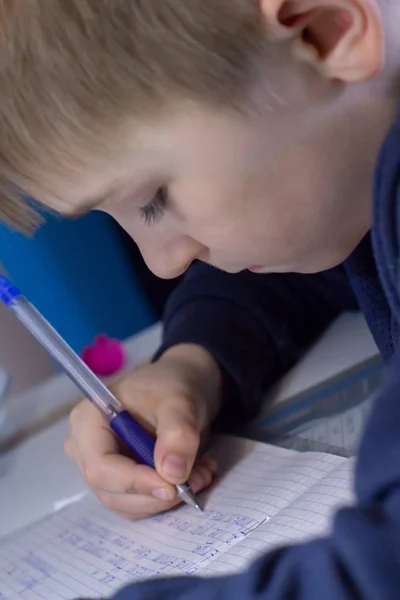전통적인 흰색 메모장 종이에 손으로 영어 단어를 쓰는 연필로 소년의 손을 클로즈업. 소년은 영어로 첫 편지를 씁니다. 자식 쓰기 — 스톡 사진