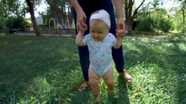 Küçük bebek yürümeyi öğreniyor. İlk Basamaklar. Ebeveynler çocuklarına yaz aylarında yeşil çimlerde ilk adımları atmayı öğretiyor. Mutlu çocukluk ve ebeveynlik kavramları. Aile sevgisi