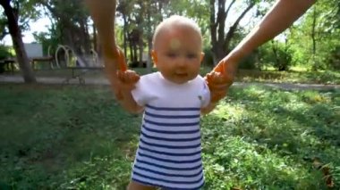 Küçük bebek yürümeyi öğreniyor. İlk Basamaklar. Ebeveynler çocuklarına yaz aylarında yeşil çimlerde ilk adımları atmayı öğretiyor. Mutlu çocukluk ve ebeveynlik kavramları. Aile sevgisi