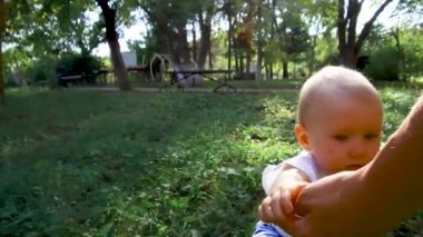 Küçük bebek yürümeyi öğreniyor. İlk Basamaklar. Ebeveynler çocuklarına yaz aylarında yeşil çimlerde ilk adımları atmayı öğretiyor. Mutlu çocukluk ve ebeveynlik kavramları. Aile sevgisi
