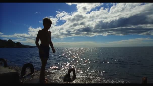 Щаслива дитина стрибає в море. Повільний рух. Щасливий маленький хлопчик стрибає у воду біля моря. Малюк піднімає бризки . — стокове відео
