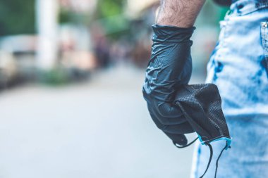 Siyah eldivenli adam elinde tıbbi bir maske tutuyor.