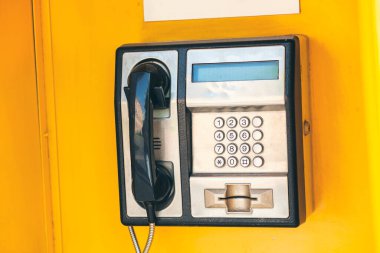 Şehirdeki bir ankesörlü telefonun sarı arka planda yakın plan görüntüsü.