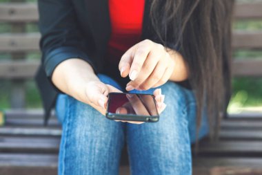 Parkta akıllı telefon kullanan genç bir kadın.