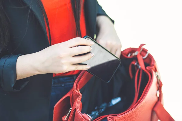 A hand put the phone in the female red leather handbag