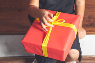 Çocuğun elinde kraft kağıdına sarılı sarı kurdeleyle bağlanmış bir hediye kutusu var. Üst manzara, tatil konsepti