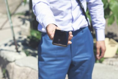 Genç bir adam sokakta elinde bir telefon tutuyor. İş adamı telefonu sokakta elinde tutuyor.