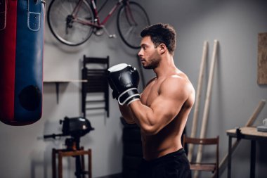 Kaslı gövdeli genç bir sporcu garajında kum torbasıyla ısınıyor..