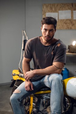Garajda, bir araba tamircisi tamir ettiği sarı bir motosikletin üzerinde oturur. Şişirilmiş şık adam..
