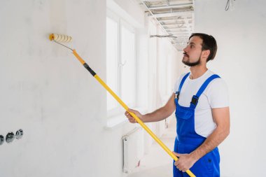 Koridorun duvarını silindirle beyaza boyayan bir işçinin yan görüntüsü