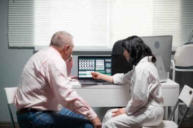 Doktor, hastasına röntgendeki ameliyat sonuçlarını gösteriyor. Dizüstü bilgisayarın görüntüsünü gösteriyor ve bazı şeyleri açıklıyor.