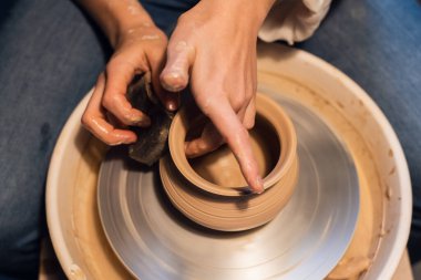 Çömlekçi bir kız çömlekçi çarkına el ve aletleriyle tencere yontuyor..